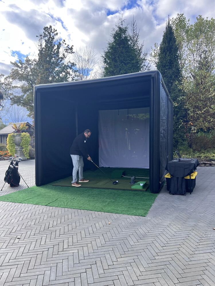 Outdoor golf simulator tent setup with a golfer swinging